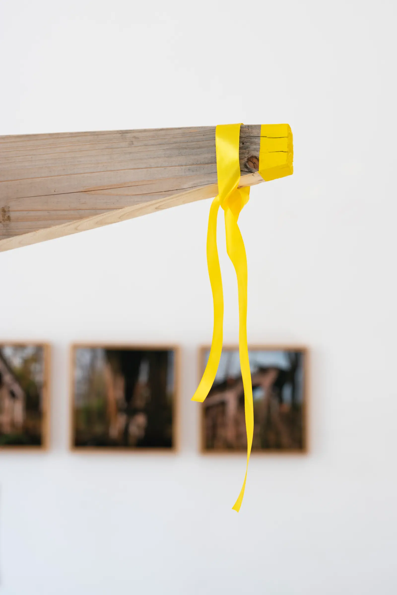 Zbliżenie na fragment instalacji – drewniany element z żółtą wstążką.