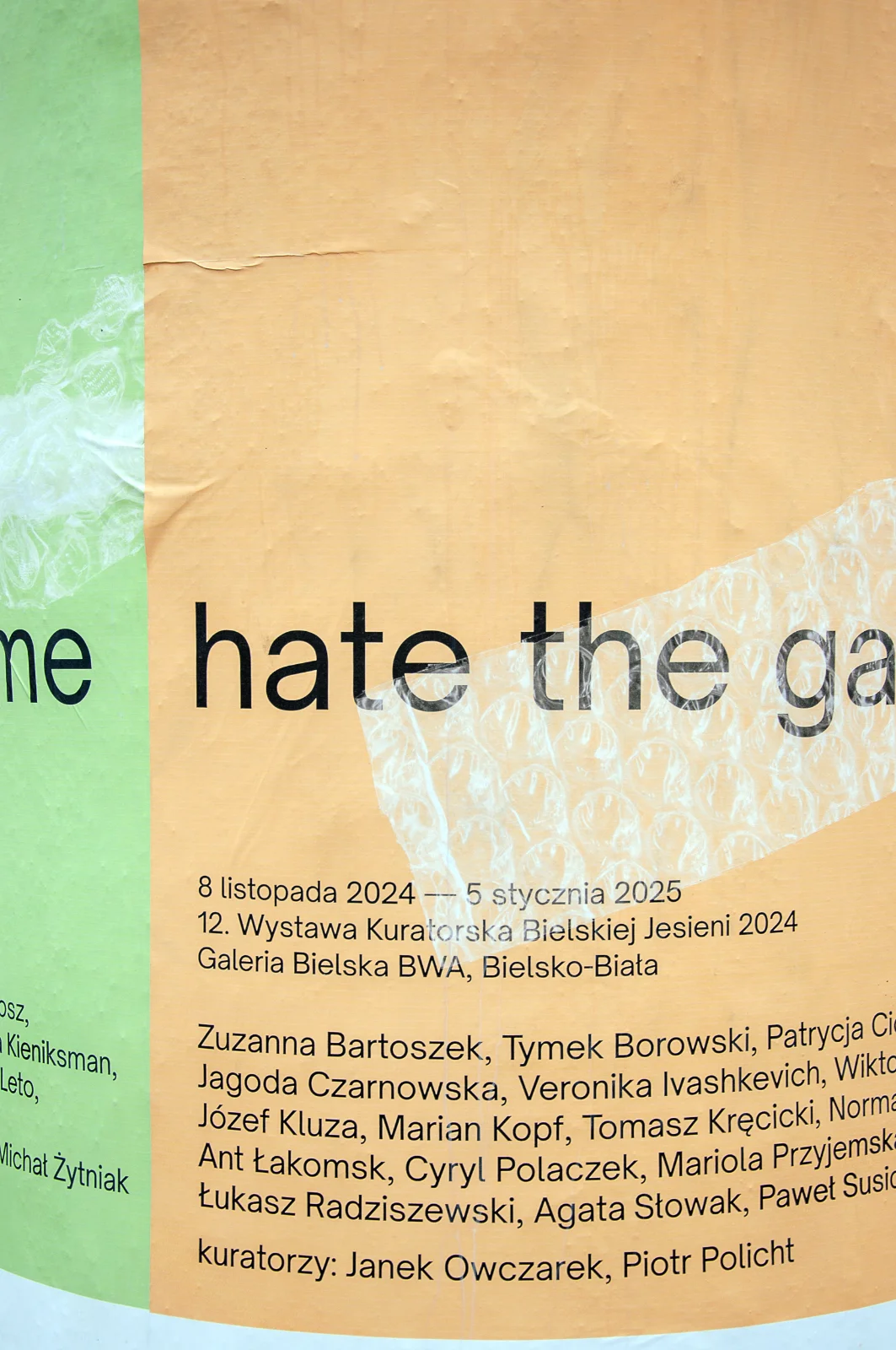 Zbliżenie na plakat wystawy z datami i nazwiskami artystów, z grafiką przedstawiającą folię bąbelkową na brzoskwiniowym tle.