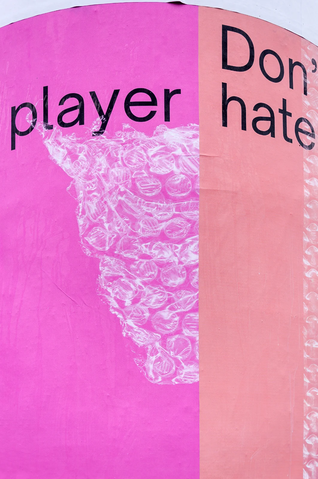 Zbliżenie na różowy plakat wystawy z fragmentem tytułu i teksturą przypominającą przezroczystą folię bąbelkową.