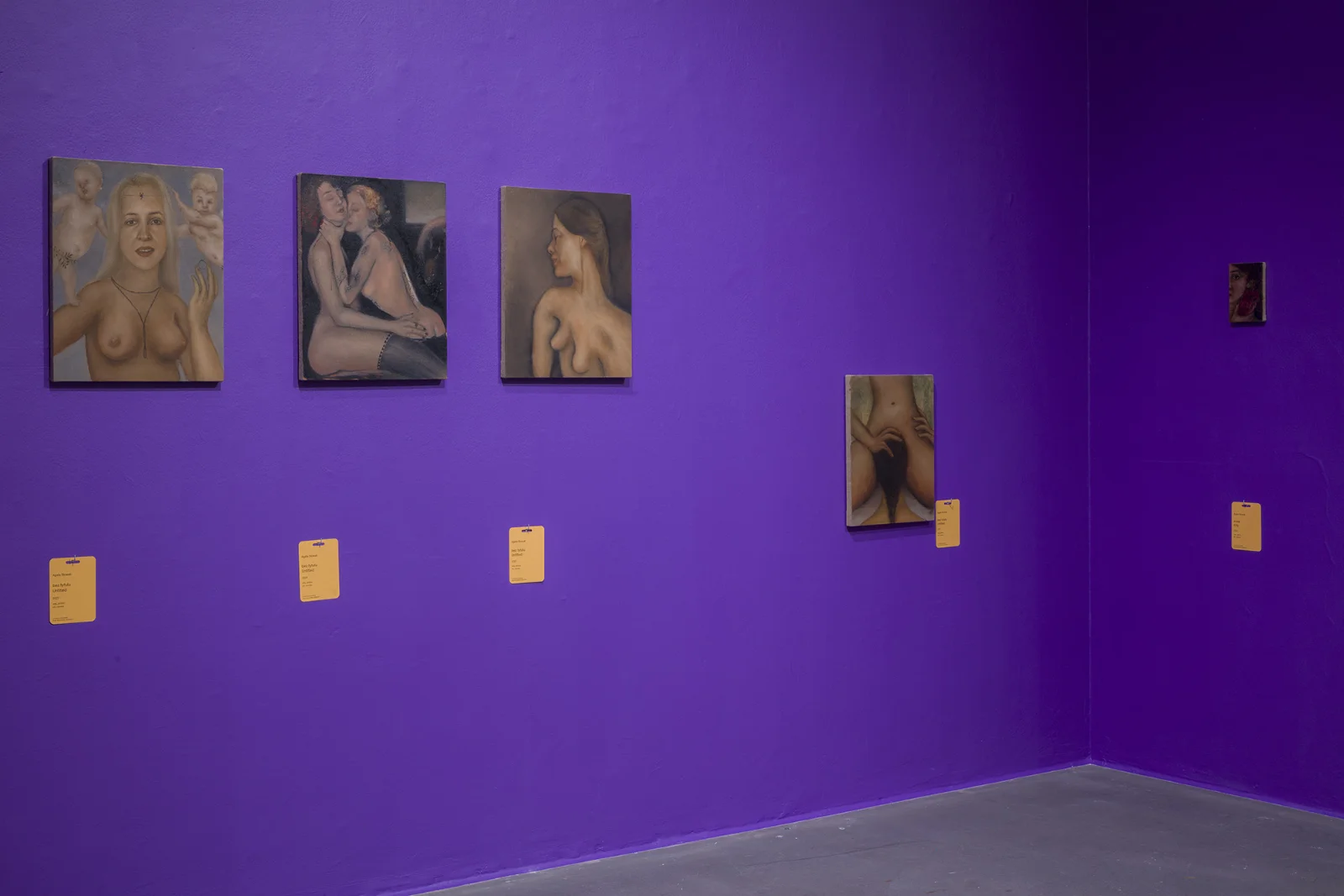 Seria czterech małych obrazów olejnych przedstawiających akty, zawieszonych w rzędzie na głębokim fioletowym tle ściany galerii z pomarańczowymi etykietami.