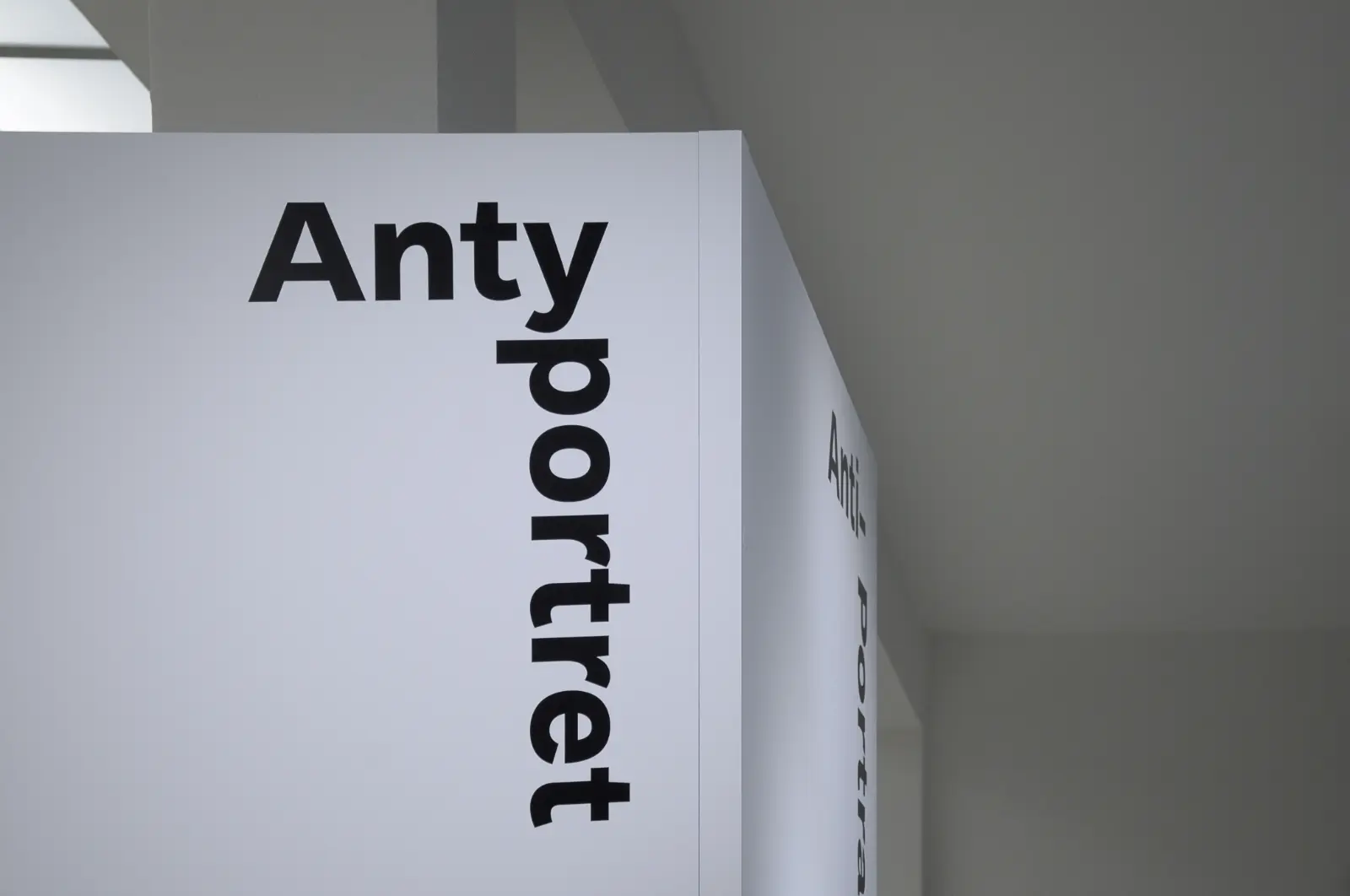 Widok wystawy „Fenomenalny. Zdzisław Beksiński”. Zbliżenie na tytuł sekcji „Antyportret”. Czarne litery na białym tle.