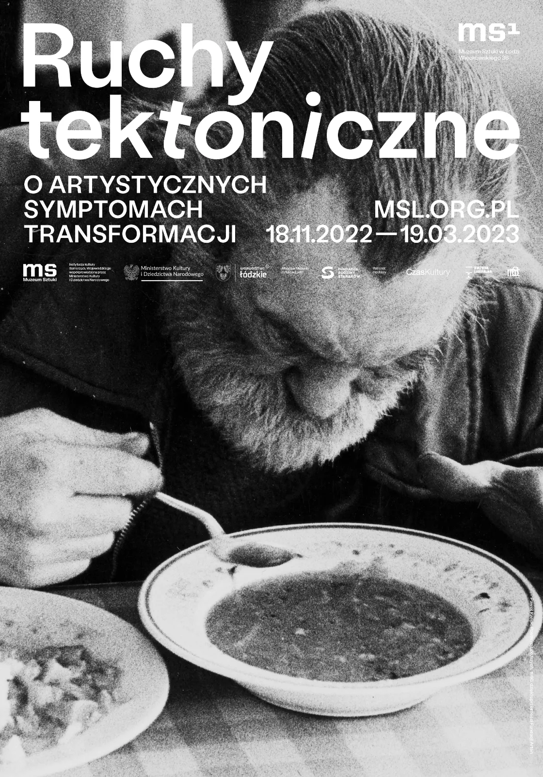 Plakat wystawy z czarno-białym zdjęciem starszego mężczyzny z brodą, który w skupieniu je zupę. Na górze biała typografia z tytułem: „Ruchy tektoniczne. O artystycznych symptomach transformacji”.