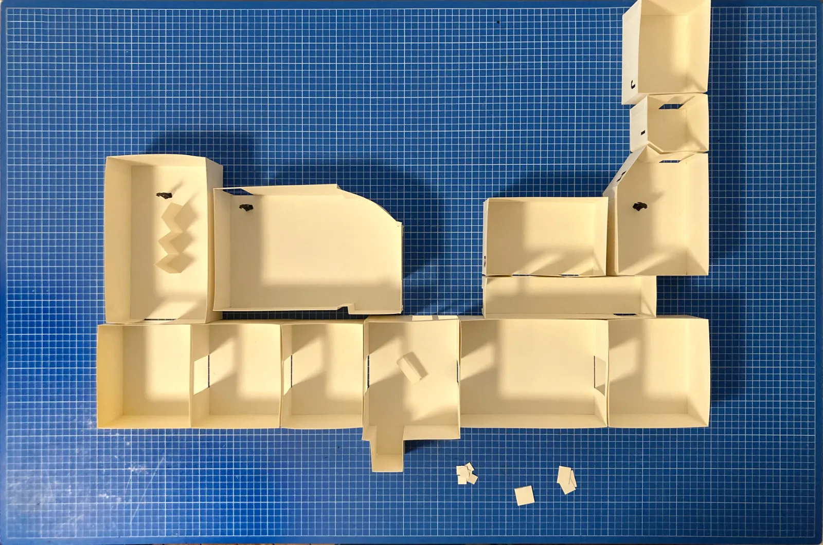 Zdjęcie makiety architektonicznej wystawy wykonane z góry (rzut). Model z białego kartonu przedstawia układ sal, umieszczony na niebieskiej macie modelarskiej z podziałką.