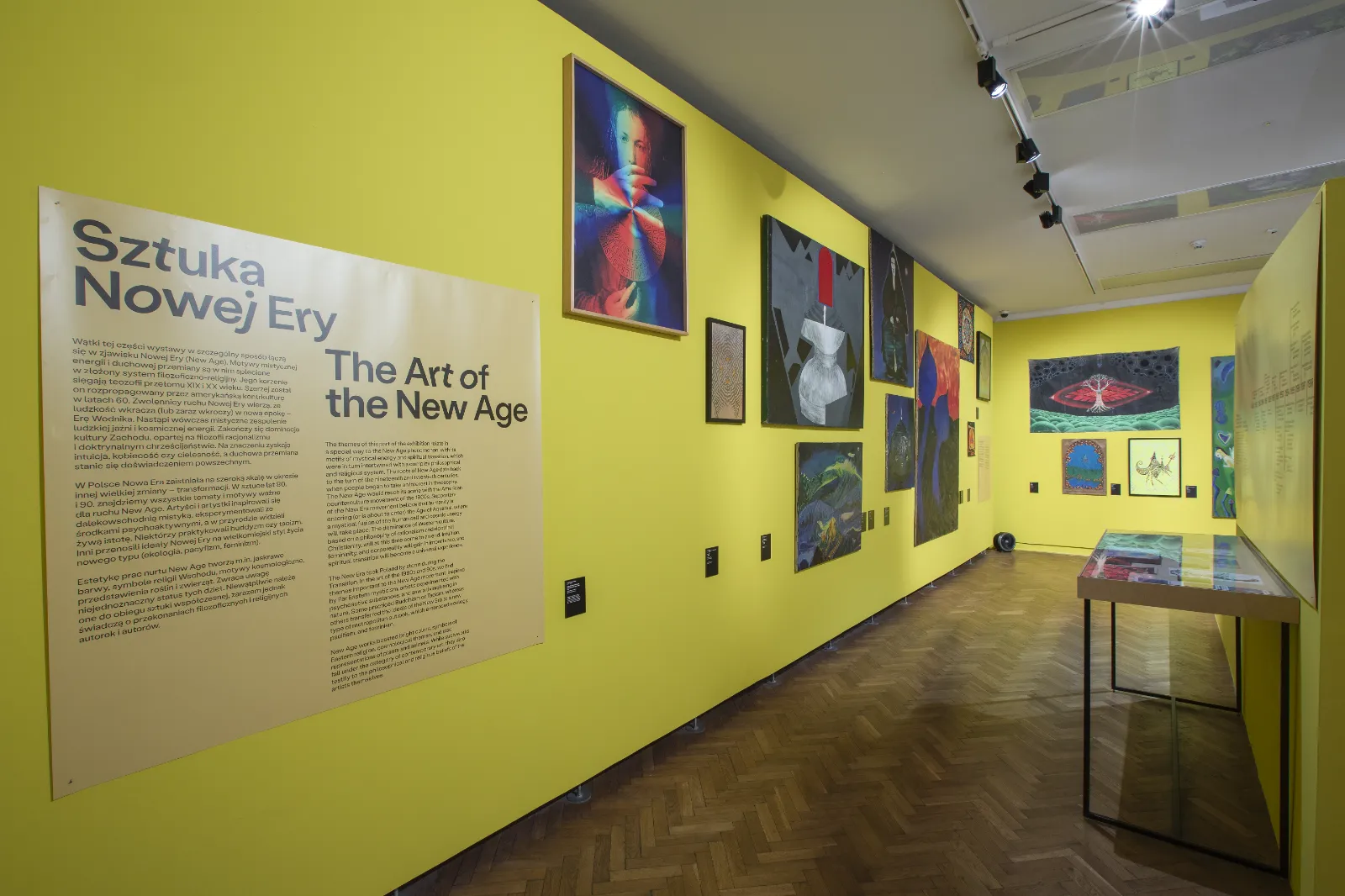 Długa, jaskrawożółta ściana zatytułowana „Sztuka Nowej Ery”. Wiszą na niej liczne, kolorowe obrazy o tematyce ezoterycznej i mistycznej.