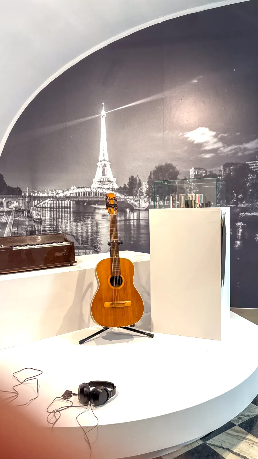 Gitara akustyczna i małe pianino wystawione na tle wielkoformatowej fototapety z wieżą Eiffla.