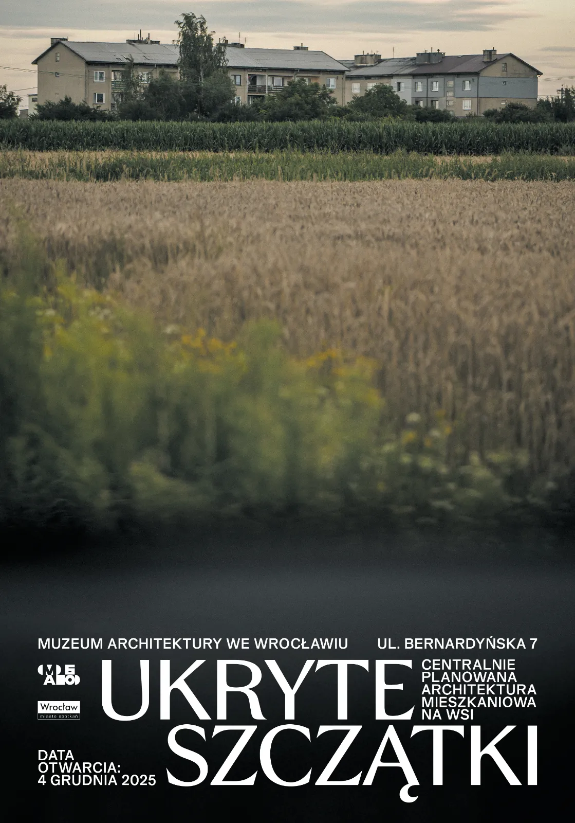 Plakat wystawy: tytuł na dole, fotografia przedstawiająca blok pośród pól na górze.