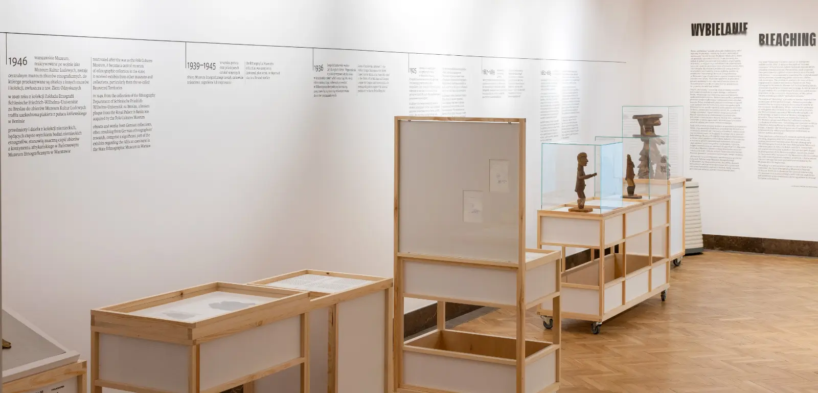 Widok wystawy. W tle tekst nadrukowany na ścianie. Na pierwszym planie gabloty z artefaktami.
