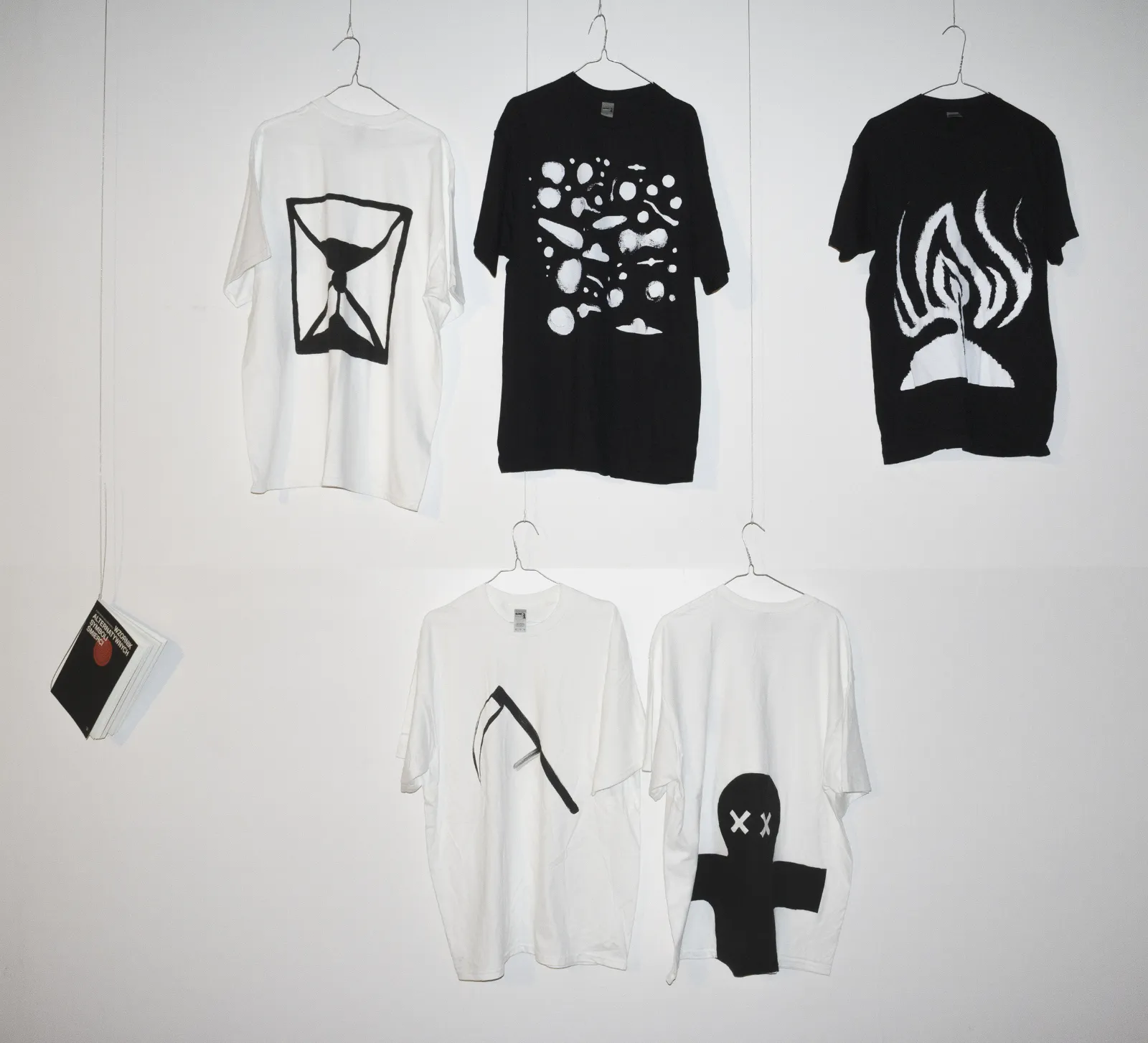 Trzy białe i dwie czarne koszulki z wybranymi symbolami wiszą na ścianie