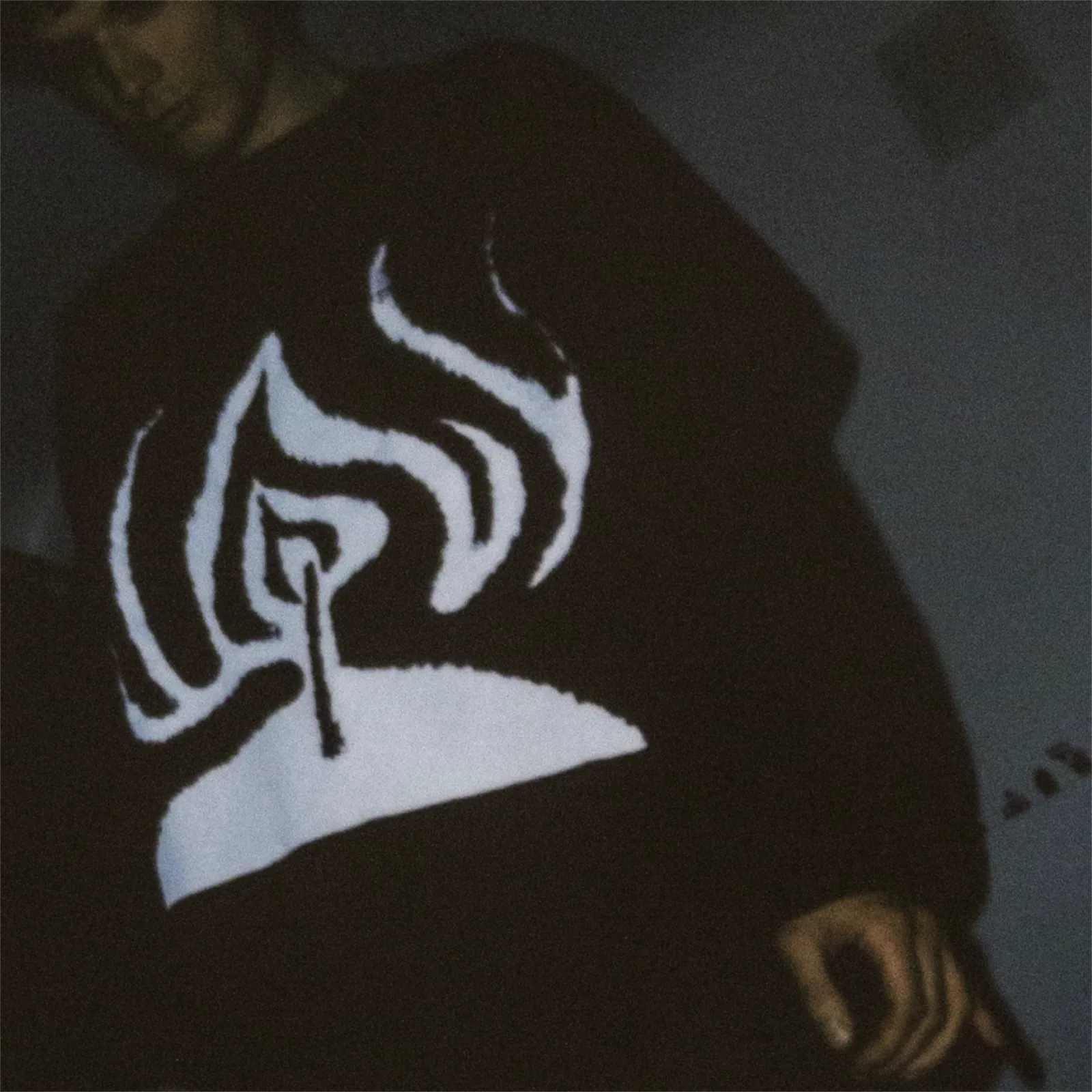 Mężczyzna ubrany w koszulkę z symbolem znicza stoi w ciemnym pokoju